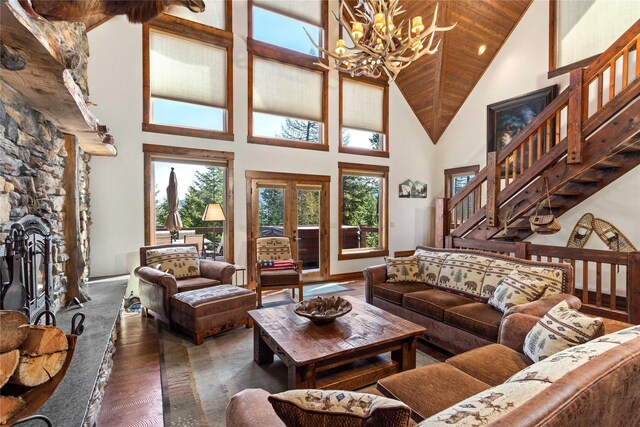 living room featuring a notable chandelier, stairway, wood finished floors, high vaulted ceiling, and a stone fireplace