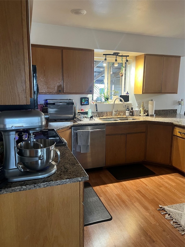 kitchen with stainless steel dishwasher, dark stone counters, a toaster, a sink, and light wood-type flooring