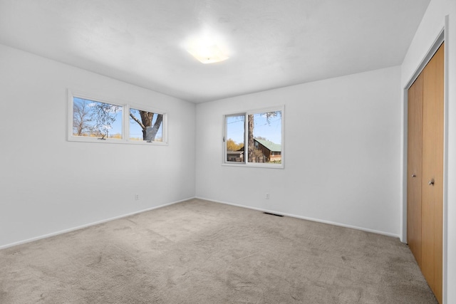 unfurnished bedroom with baseboards, visible vents, a closet, and light colored carpet