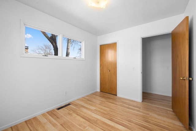 unfurnished bedroom featuring visible vents, a closet, light wood-style flooring, and baseboards