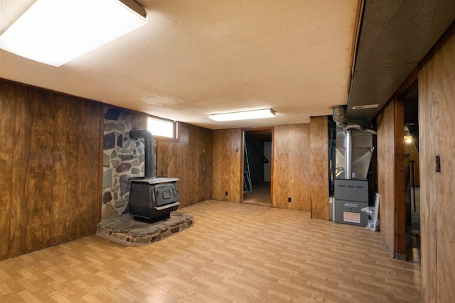 basement with wood walls, light wood finished floors, and a wood stove