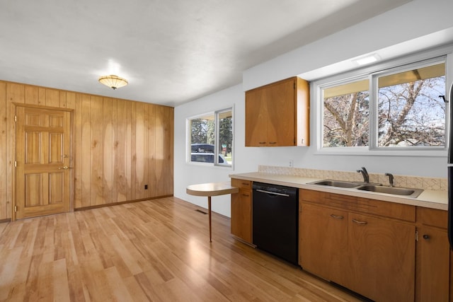 kitchen with black dishwasher, light countertops, light wood-style flooring, and a sink