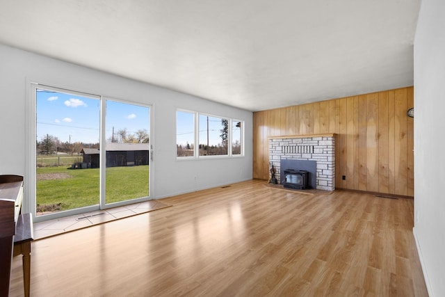 unfurnished living room with a wood stove, wood walls, wood finished floors, and baseboards
