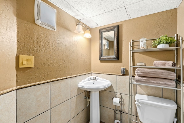 11 Wilson Butte Rd, Great Falls, MT 59405 - bathroom featuring toilet, a textured wall, tile walls, a paneled ceiling, and wainscoting