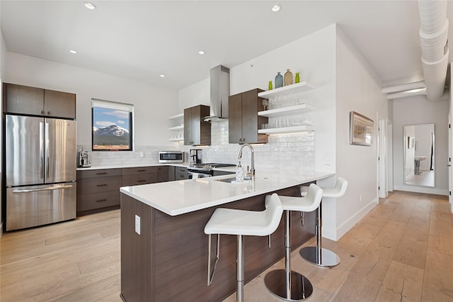 kitchen with exhaust hood, appliances with stainless steel finishes, open shelves, a peninsula, and a breakfast bar
