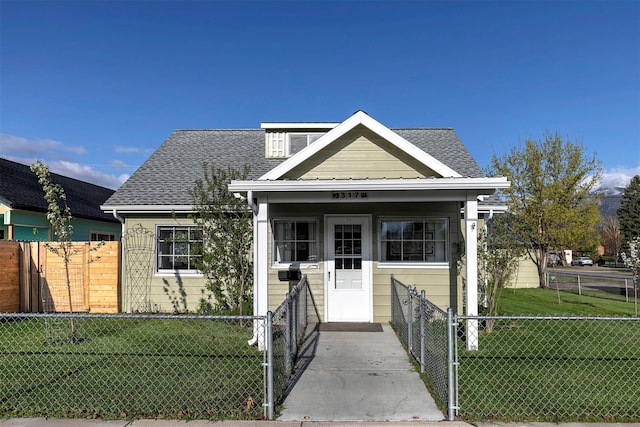 bungalow-style home featuring a fenced front yard, a shingled roof, and a front lawn
