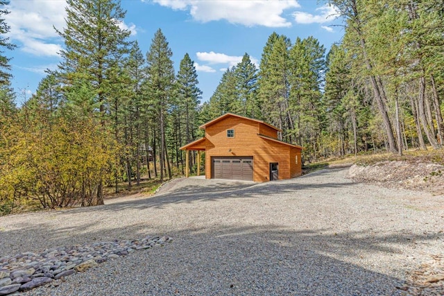 exterior space with a detached garage, driveway, a wooded view, and an outdoor structure