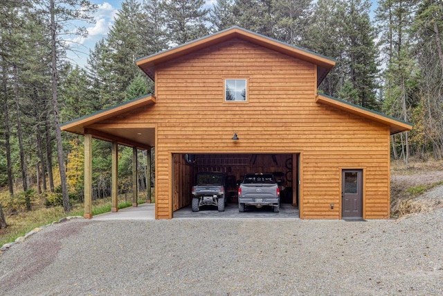 garage featuring a detached garage, driveway, and a forest view