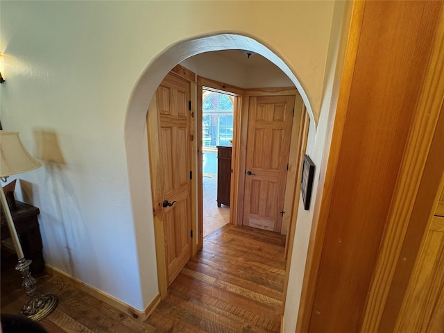 corridor featuring arched walkways, baseboards, and wood finished floors