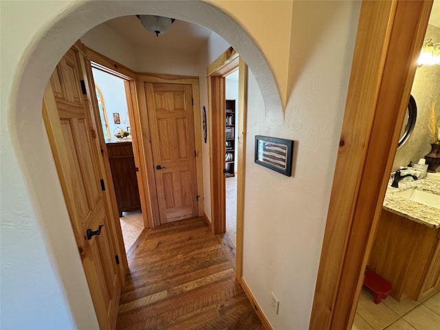 hall featuring baseboards, arched walkways, and a sink
