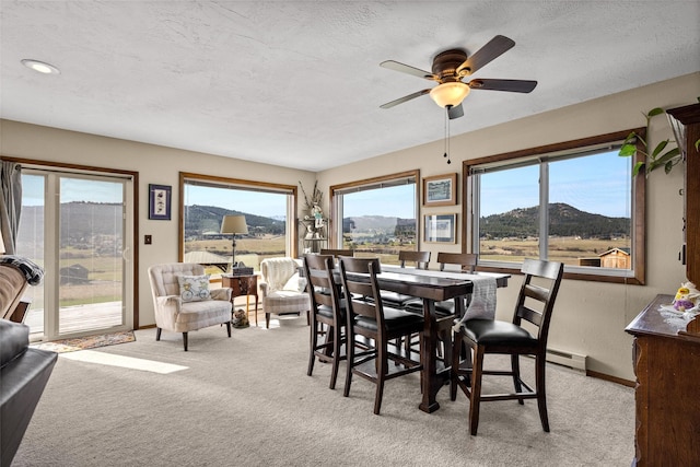 carpeted dining room featuring a ceiling fan, a textured ceiling, a baseboard heating unit, and a wealth of natural light