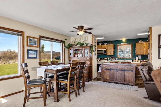 dining room with baseboards, ceiling fan, a wealth of natural light, and light carpet