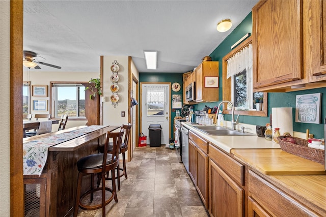 kitchen with brown cabinets, a sink, light countertops, a ceiling fan, and stainless steel microwave