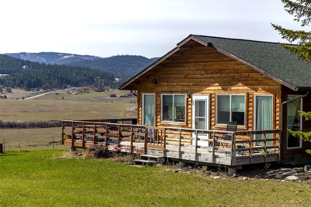 back of property with a deck with mountain view, a shingled roof, and a yard