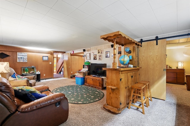 carpeted living room with wood walls, a barn door, and stairway