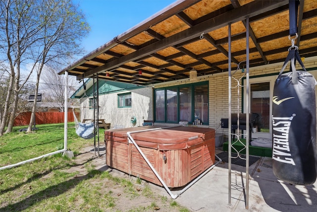 rear view of property featuring a hot tub, brick siding, a yard, and fence