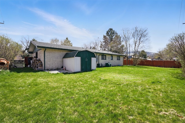 rear view of property with a storage shed, an outbuilding, brick siding, fence, and a yard