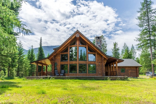 rear view of house with a lawn, a mountain view, log exterior, and a chimney