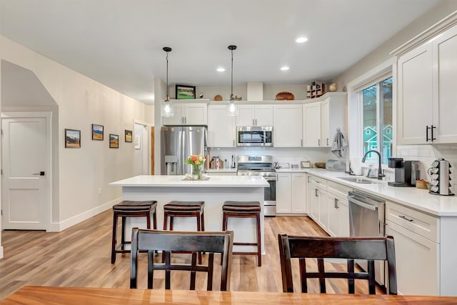 kitchen with baseboards, light wood-type flooring, white cabinets, a sink, and stainless steel appliances
