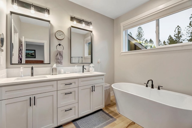 bathroom featuring double vanity, a sink, wood finished floors, and a soaking tub
