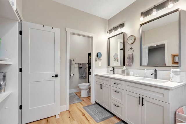 full bathroom with a sink, double vanity, toilet, and wood finished floors