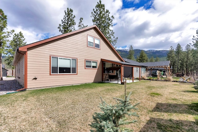 rear view of property with a lawn, a mountain view, and a patio area