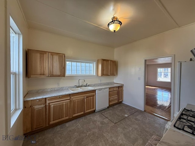 kitchen with brown cabinetry, white appliances, baseboards, light countertops, and a sink