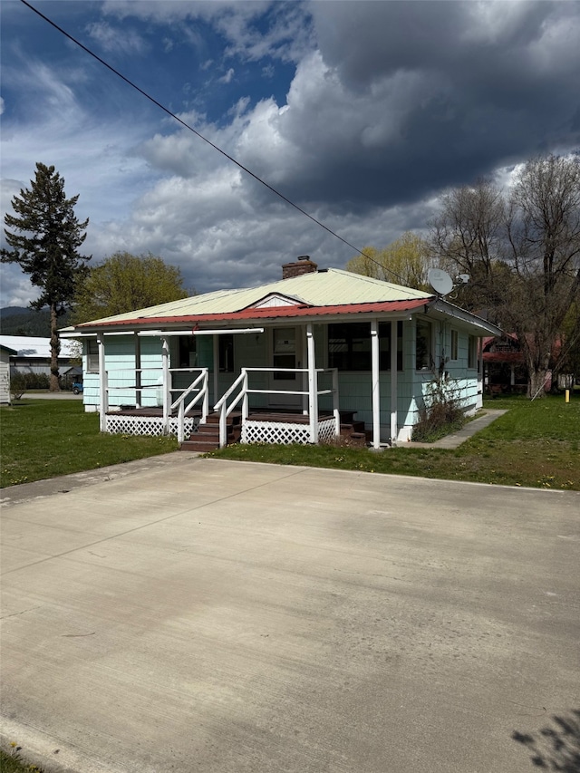 view of front of property featuring a porch, a front lawn, a chimney, and metal roof