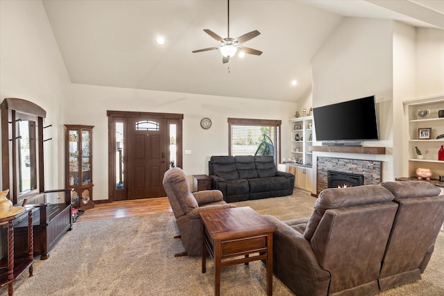 living room with ceiling fan, light colored carpet, light wood finished floors, a fireplace, and high vaulted ceiling