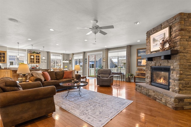 living room featuring recessed lighting, ceiling fan, hardwood / wood-style flooring, and a stone fireplace