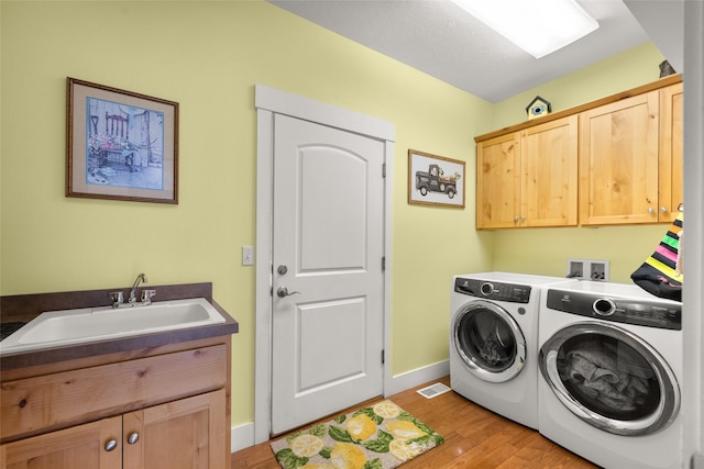clothes washing area featuring cabinet space, a sink, light wood-type flooring, visible vents, and washing machine and dryer