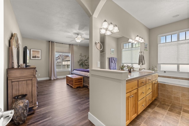 bathroom with vanity, wood finished floors, a textured ceiling, a ceiling fan, and tiled bath