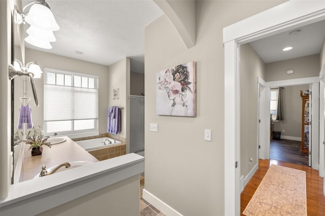 bathroom with a sink, baseboards, wood finished floors, a bath, and a stall shower