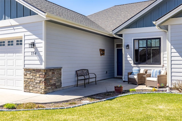 doorway to property featuring stone siding, a shingled roof, board and batten siding, an attached garage, and a yard