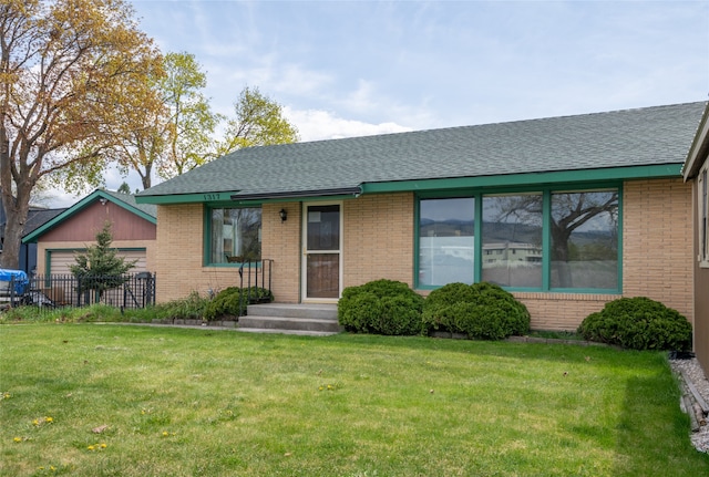 ranch-style home featuring brick siding, a front yard, and roof with shingles