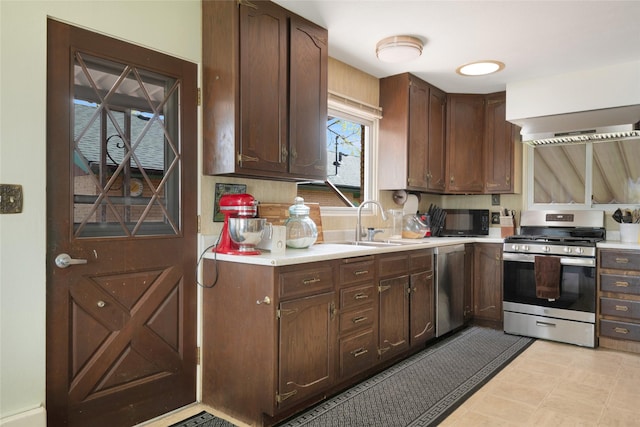 kitchen featuring dark brown cabinetry, a sink, light countertops, stainless steel appliances, and wall chimney exhaust hood