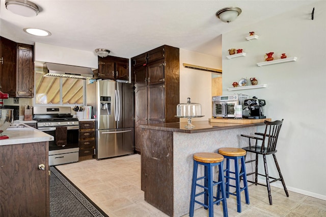 kitchen featuring dark brown cabinetry, a kitchen breakfast bar, stainless steel appliances, baseboards, and a peninsula