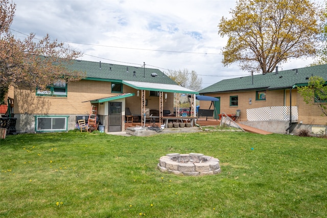 back of house with brick siding, an outdoor fire pit, and a yard