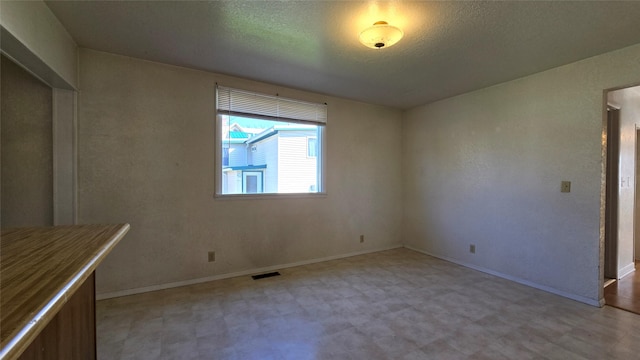 unfurnished dining area featuring baseboards, a textured ceiling, light floors, and visible vents