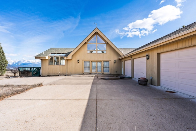 chalet / cabin featuring an attached garage, roof with shingles, french doors, and concrete driveway