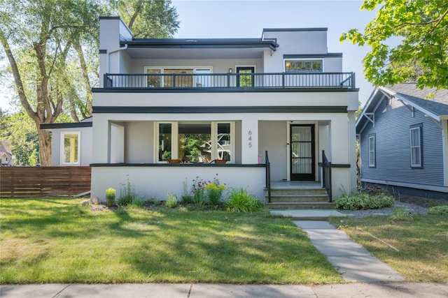 view of front facade featuring a porch, fence, a balcony, a front lawn, and stucco siding
