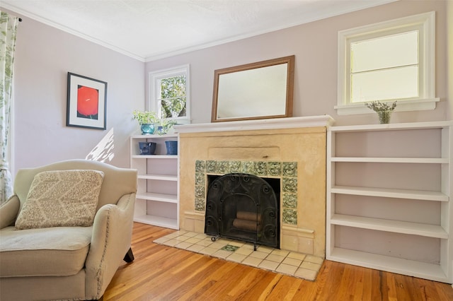 sitting room with a tiled fireplace, ornamental molding, and wood finished floors