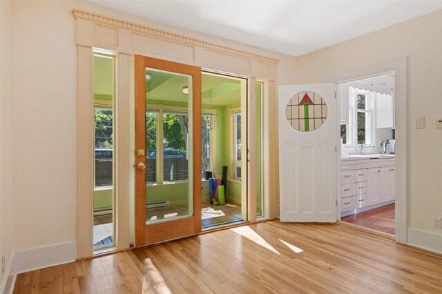 doorway to outside with a baseboard radiator, plenty of natural light, light wood finished floors, and a sink