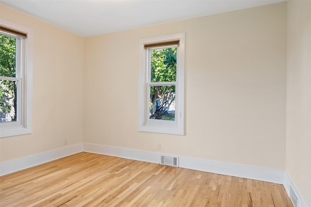 empty room featuring baseboards, a wealth of natural light, wood finished floors, and visible vents