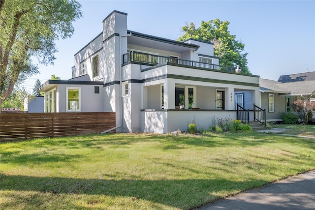 exterior space featuring a lawn, stucco siding, a balcony, and fence