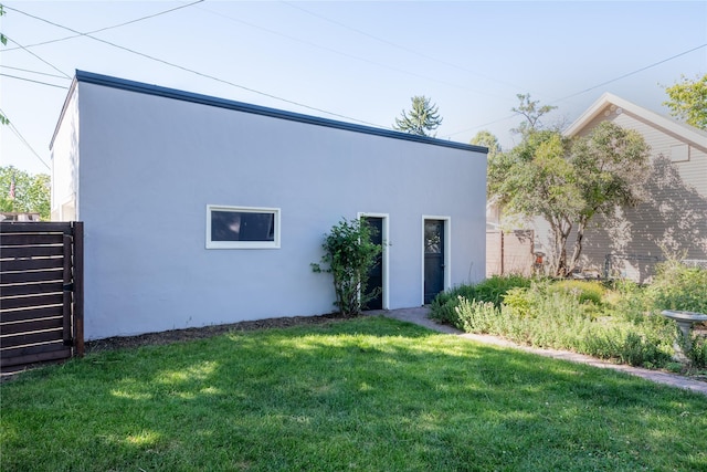 back of house featuring a lawn, fence, and stucco siding