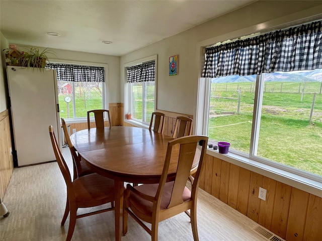 dining space with wooden walls, visible vents, wainscoting, and light wood finished floors