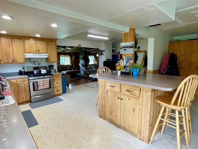 kitchen with stainless steel gas stove, light countertops, recessed lighting, a kitchen bar, and under cabinet range hood