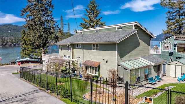 rear view of property featuring fence private yard, a shingled roof, a lawn, and a water view
