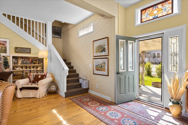 foyer featuring baseboards, wood walls, stairway, and light wood-style floors